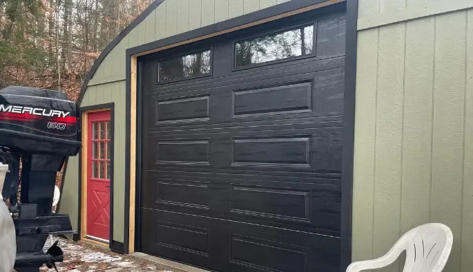A green shed with a large black garage door featuring small windows at the top.