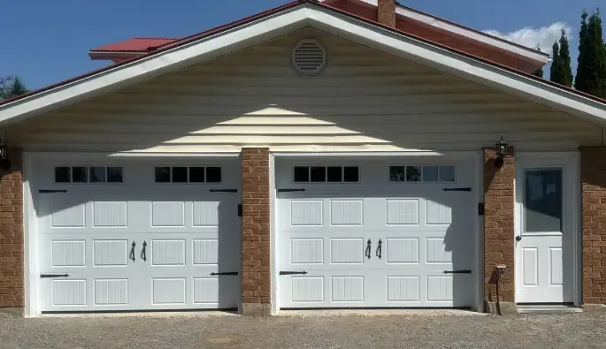 A garage with two white doors featuring small upper windows, flanked by brick siding.