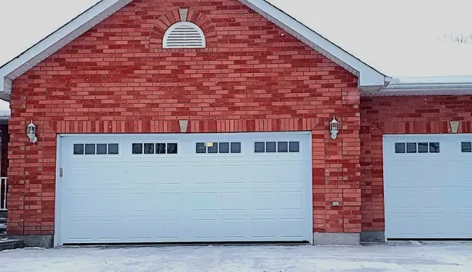 Red brick garage with two white garage doors, each featuring six small windows at the top.